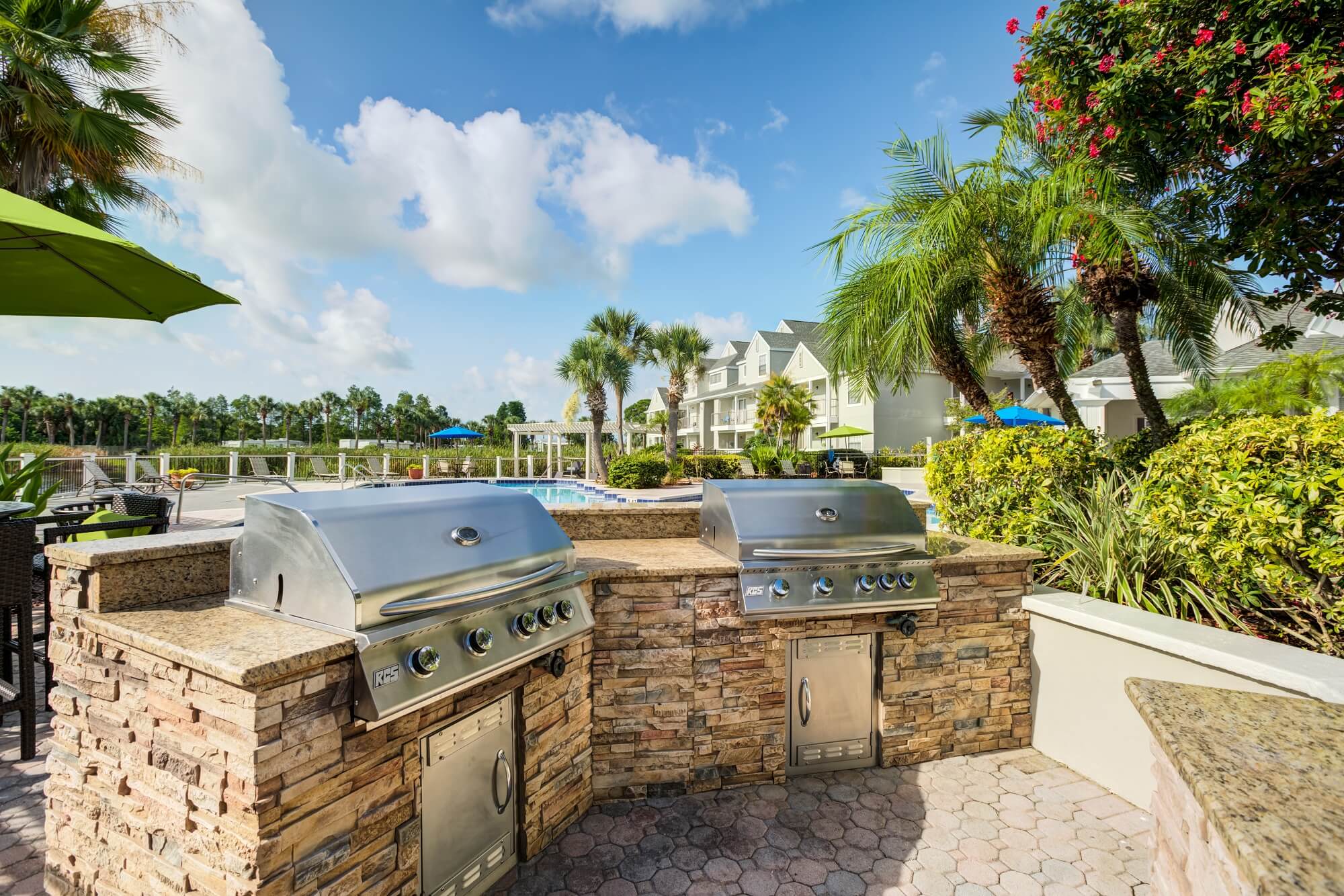 two 4 burner grills with stone countertops near the pool.